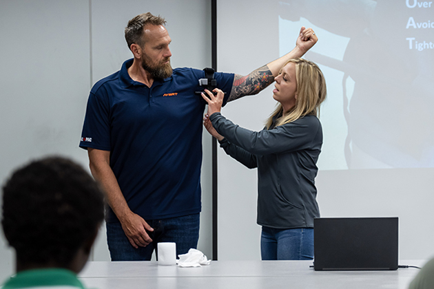 A woman demonstrates how to apply a tourniquet to a man's upper arm